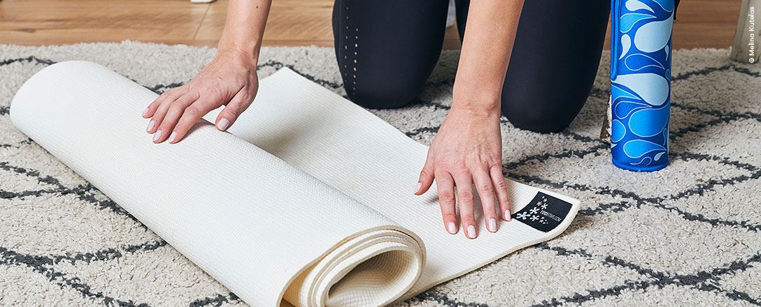 Frau rollt Sportmatte zuhause aus