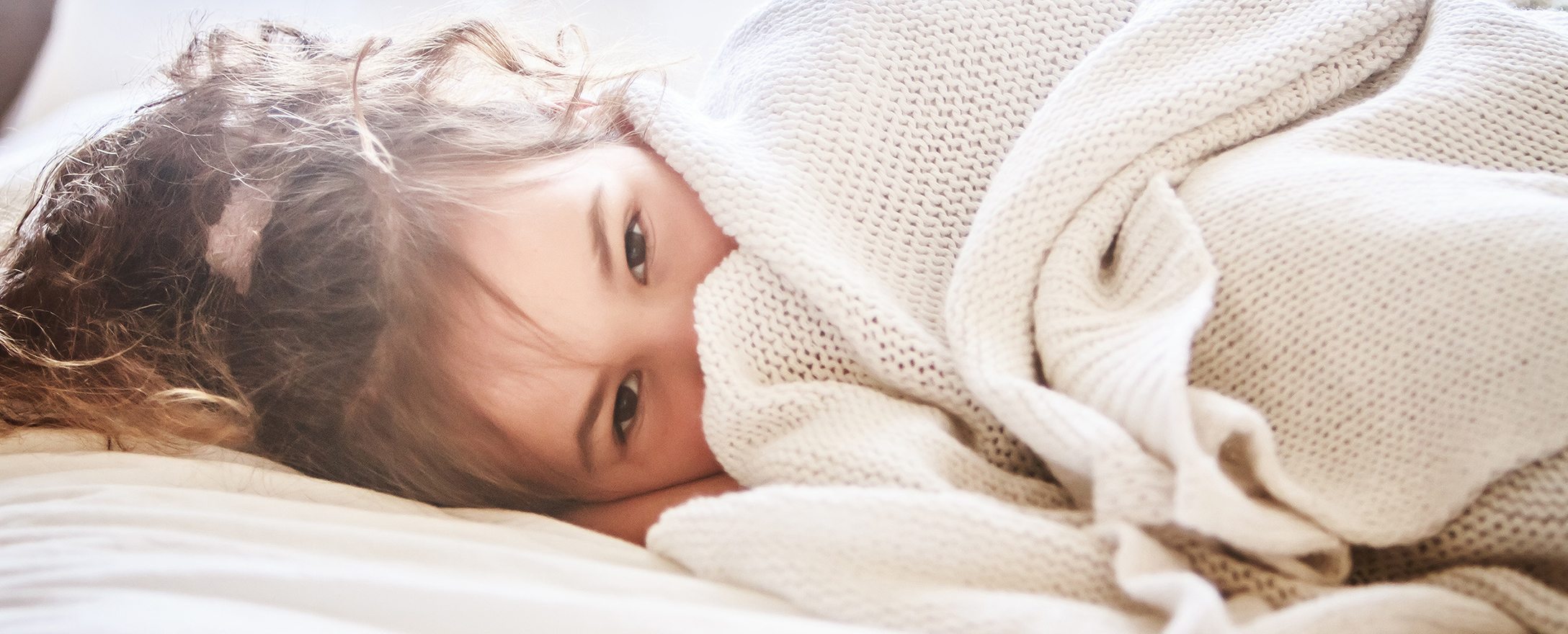 Kind liegt im Bett unter einer Decke