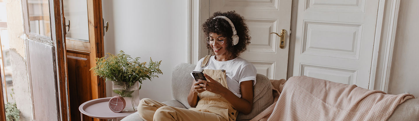 Frau mit Kopfhörer und Smartphone auf Couch