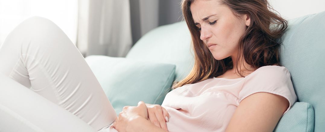Junge Frau am Sofa mit den Händen am Bauch